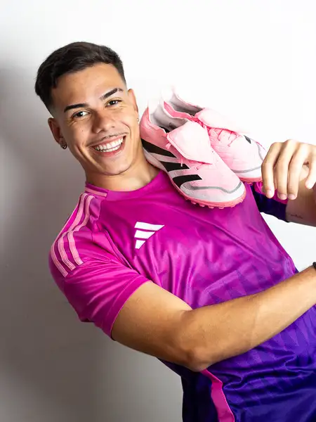 Dudu Footz sorrindo com um par de chuteiras rosas sobre o ombro
